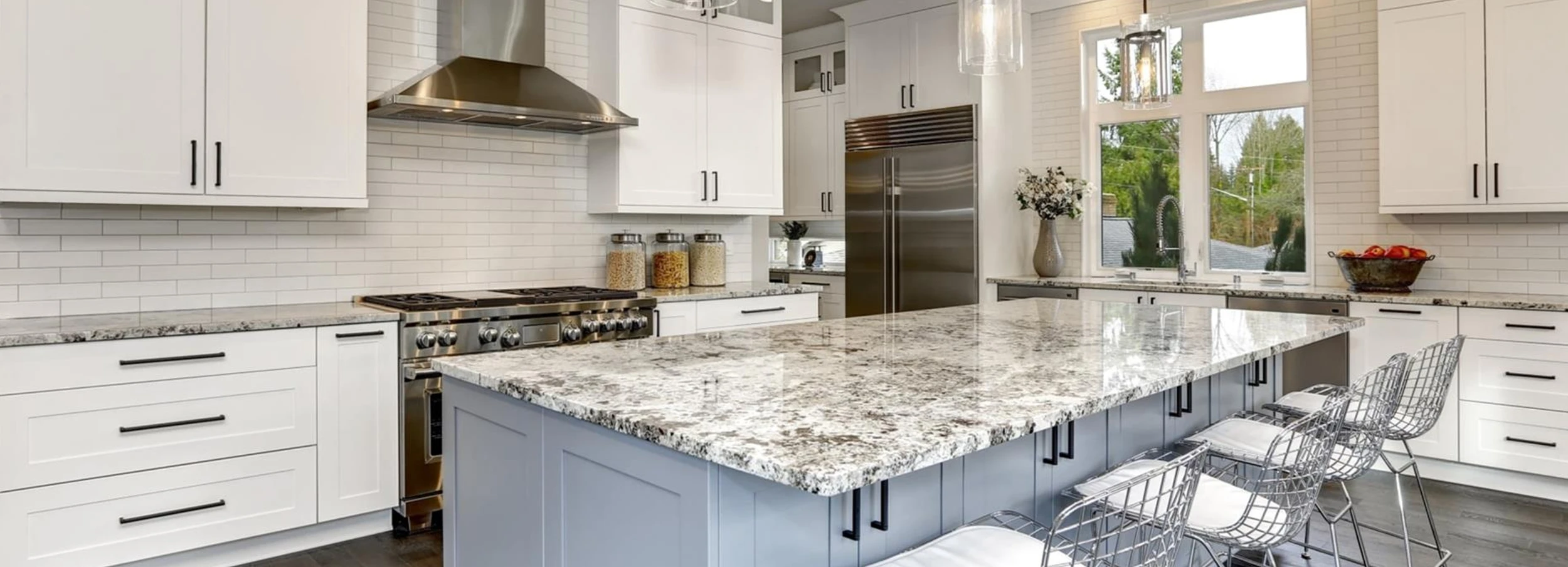 Gray marble top kitchen island in center of large, bright modern kitchen with white cabinets.