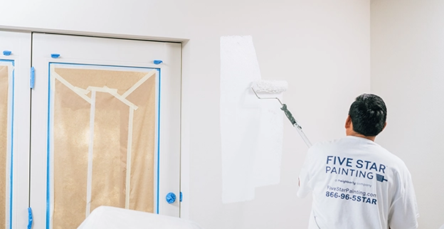 A Five Star Painting technician painting a wall white.