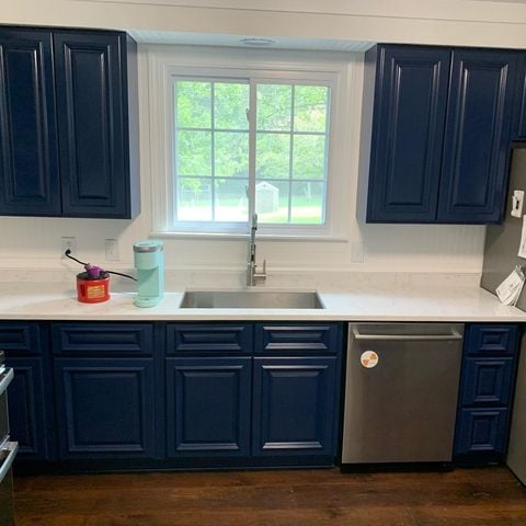 Blue kitchen cabinets with white counter top with window over sink