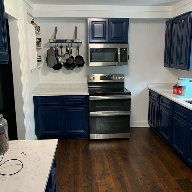 Blue kitchen cabinets with white countertops and stainless steel appliances with dark wood floors