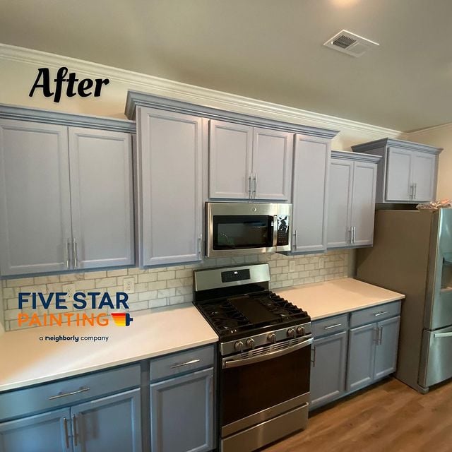 Cabinets painted light grey with silver accent handles with brick backsplash and silver and black appliances