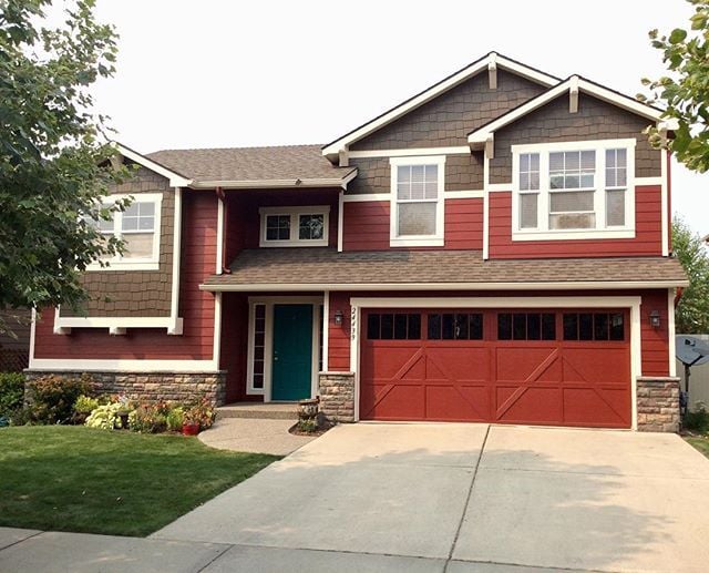 Professional painters applying a fresh coat of red paint to exterior siding and garage, enhancing curb appeal and protecting the home from the elements