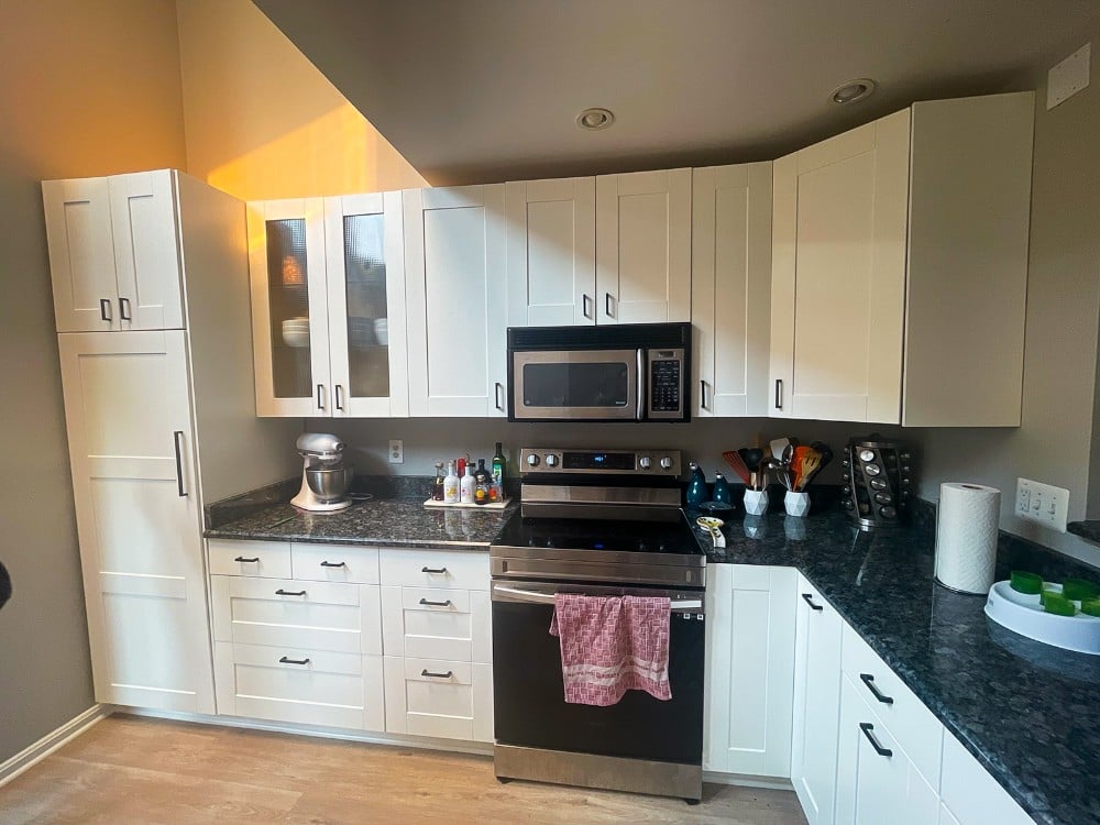 This kitchen features newly painted white cabinets that were originally stained wood. The update brightens the space, enhancing the modern look with granite countertops and stainless steel appliances.