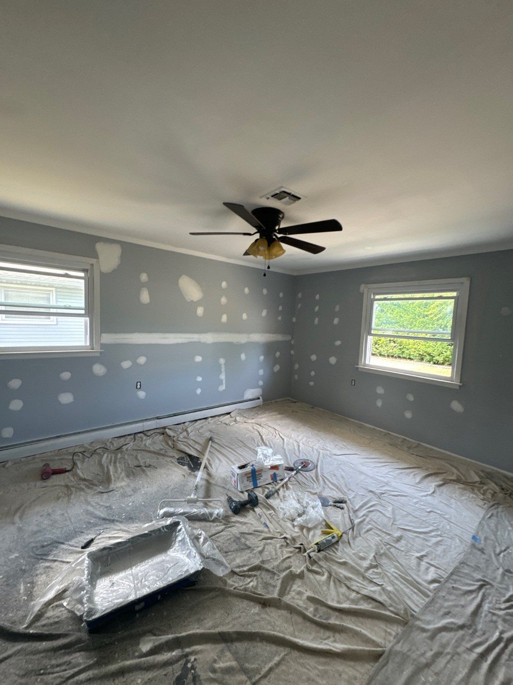 Room under preparation for painting, with walls being patched and sanded. Tools and drop cloths are visible on the floor, showcasing the attention to detail in prepping the space for a professional paint job.