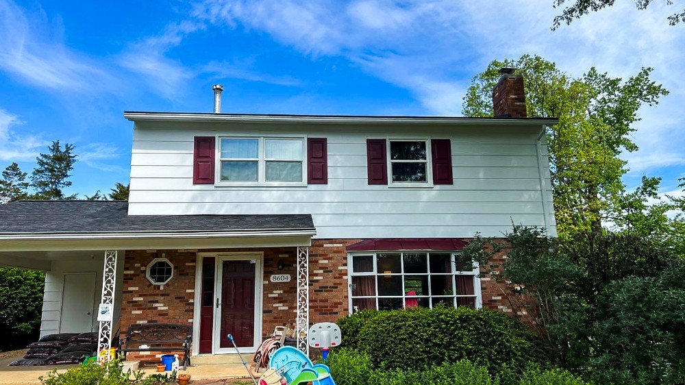 The house in the photo features a fresh, clean paint job with white siding and maroon shutters that provide a sharp contrast. The updated exterior gives the home a crisp, inviting appearance under a bright blue sky.