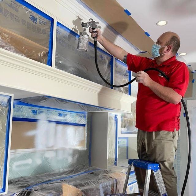 painter spray painting cabinets white