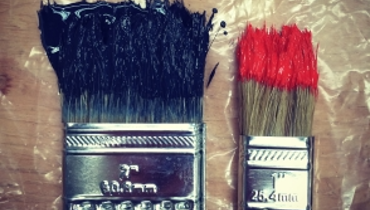 Photo of two used paint brushes resting on plastic covered wooden table