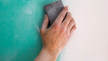 Person hand sanding drywall to prep for painting