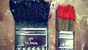 Photo of two used paint brushes resting on a plastic covered wooden table.