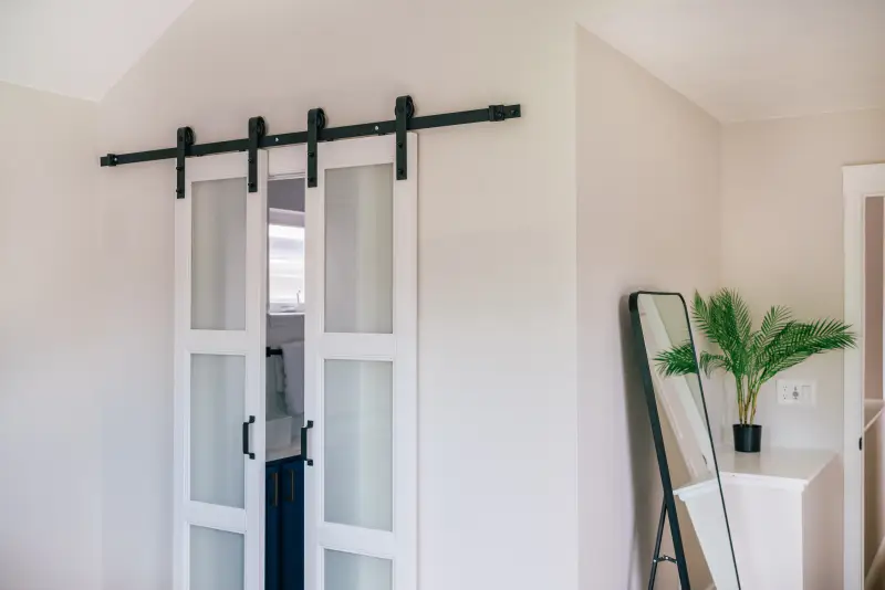 Split barn door opening up to interior bathroom. Doors are painted white with black metal slider.