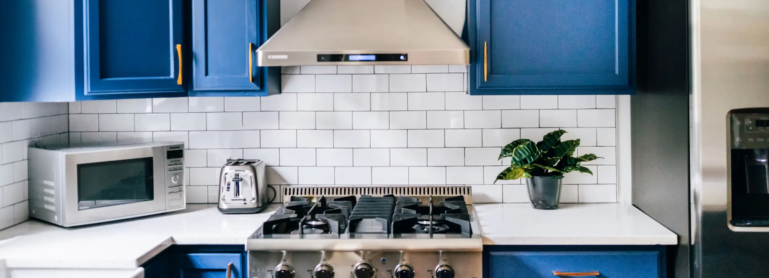 Modern kitchen with white ceramic tile wall and bright blue cabinets.