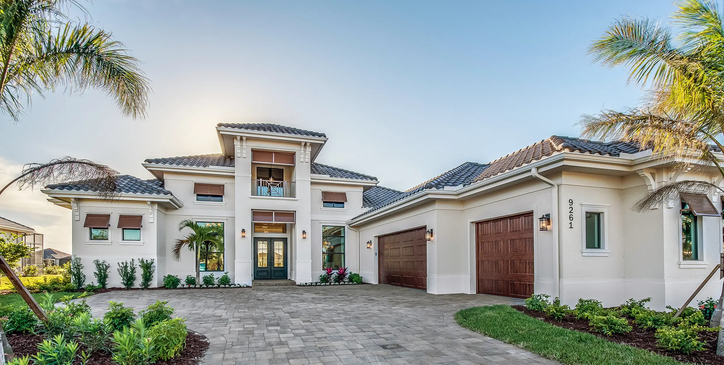 Sunny Florida home with two car garage and entrance surrounded by small palm trees.