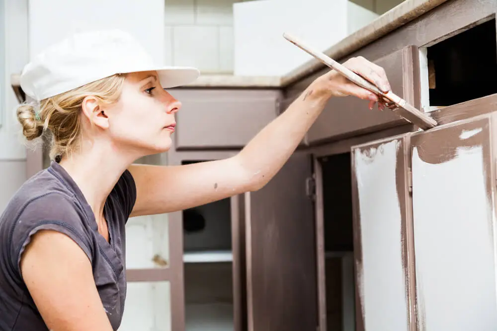 Woman painting kitchen cabinets.