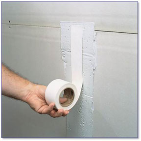 Hand holding drywall tape against the wall.