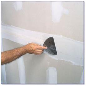 Hand showing joint knife smoothing drywall.