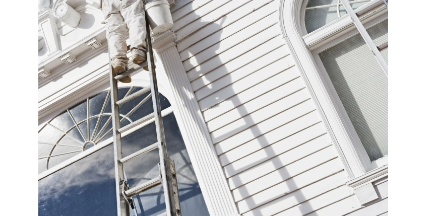 Exterior of a home being painted by a painter on a ladder.