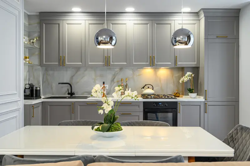 Kitchen interior with gray cabinets, marble walls, and a minimalist table with a white flower.