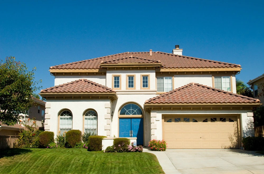 Photo of the front of a large two story house with an attached garage and a green, manicured lawn.