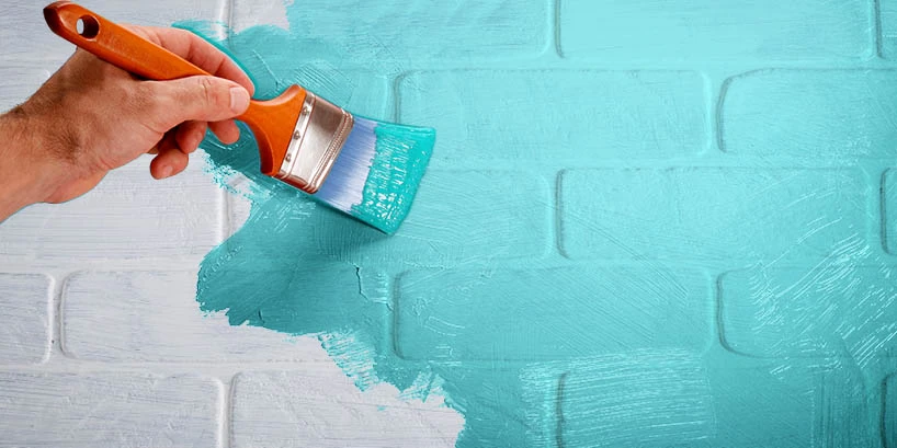 Photo of someone painting a white brick wall turquoise.