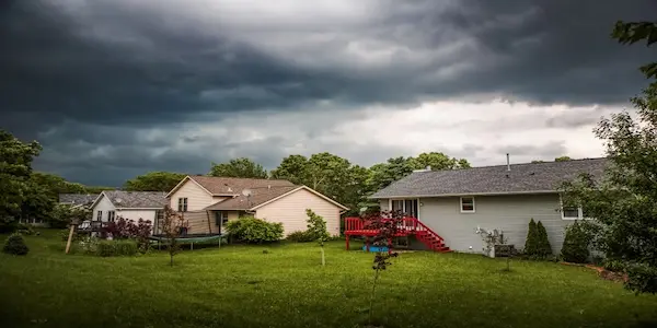 Grassy backyard and several homes under cloudy sky..