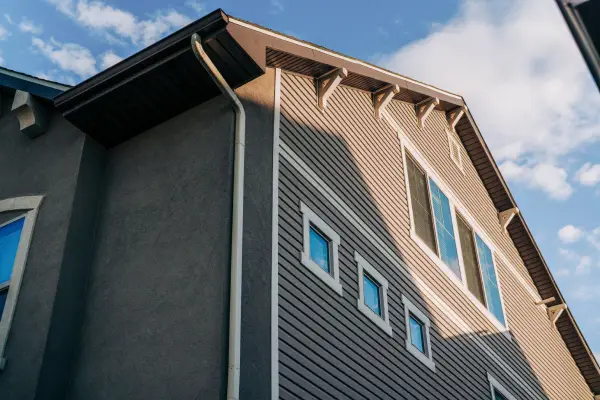 A brown house from an angle below with one side as vinyl siding and white trim. The other side of the home is stucco.