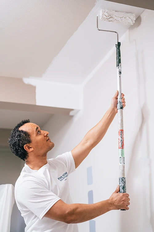 A Five Star Painting house painter using a roller to paint a ceiling.