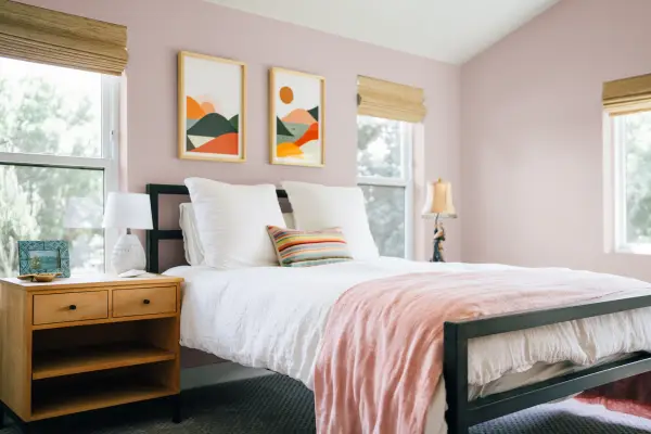 Bedroom interior painted with light pink walls and bedding with light wood furniture and vibrant earthy decor.