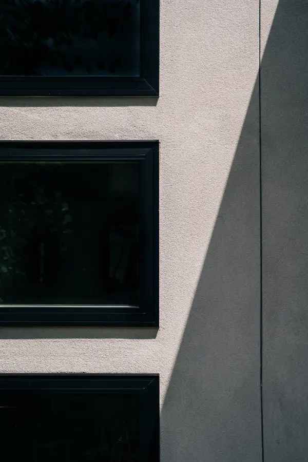 Close-up shot of residential stucco siding with angled shadow. Windows are tinted and trim painted black.