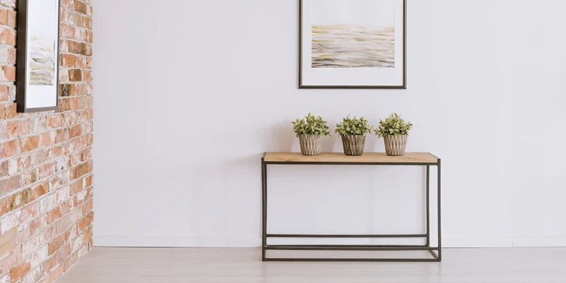 Photo of a small table with three potted plants, a brick wall, and two framed pictures.